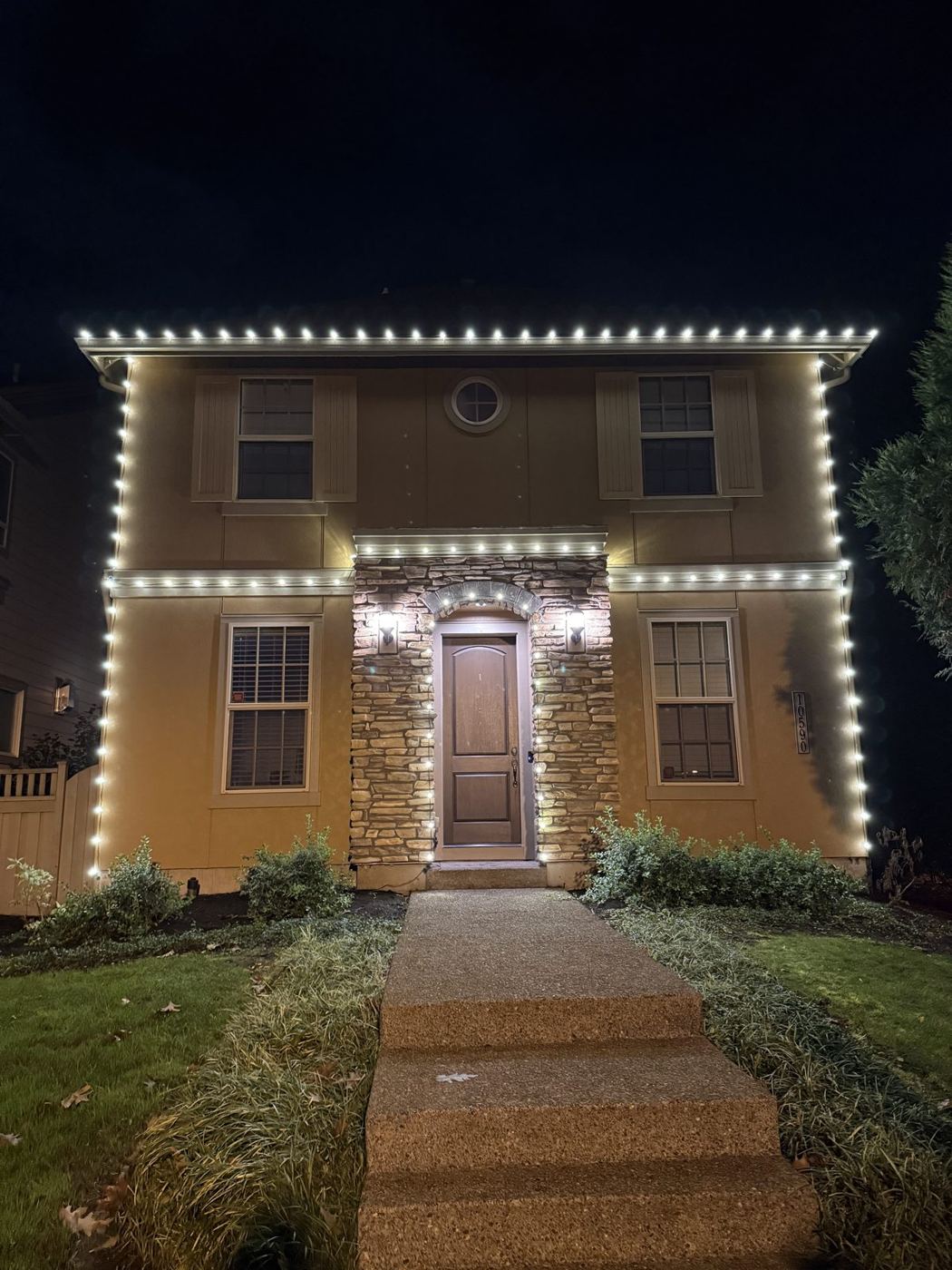 Two-story home outlined in warm white lights above a lit entry walkway